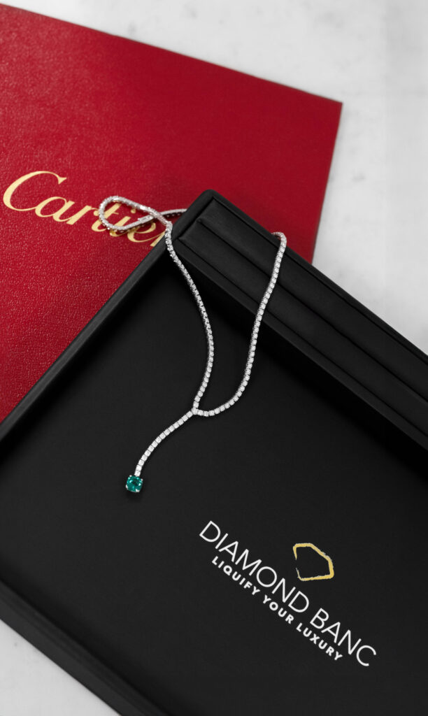 Cartier diamond necklace with an emerald main stone displayed on a Diamond Banc branded jewelry pad, with a Cartier folder in the background. This image showcases the type of luxury jewelry, but not limited to, jewelry Diamond Banc in Boca Raton is interested in purchasing. 