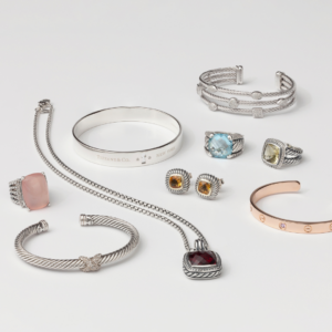 Collection of luxury designer jewelry from the premier luxury jewelry buyer in West Palm Beach, featuring Tiffany & Co. and Cartier bracelets, gemstone rings, cable-inspired cuffs, and pendant necklaces in silver and gold.